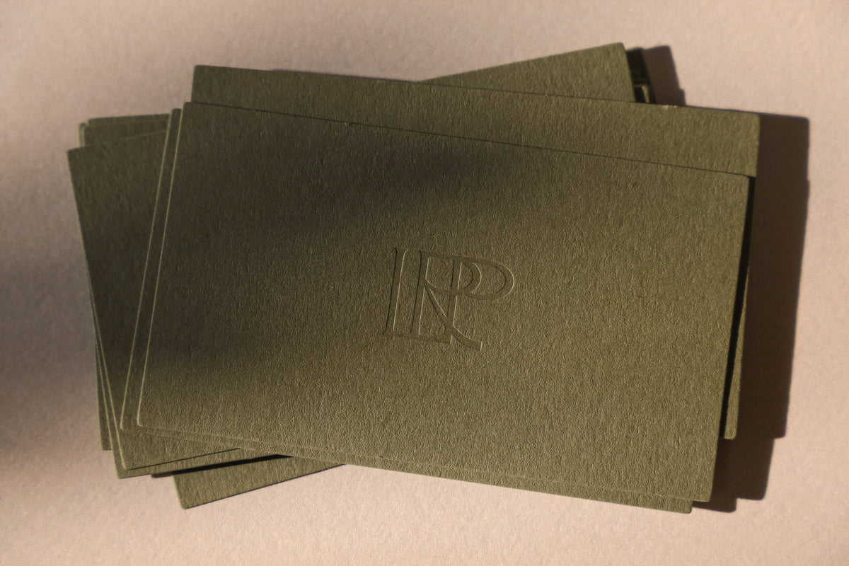 Stack of green envelopes with a blind debossed logo on a beige background