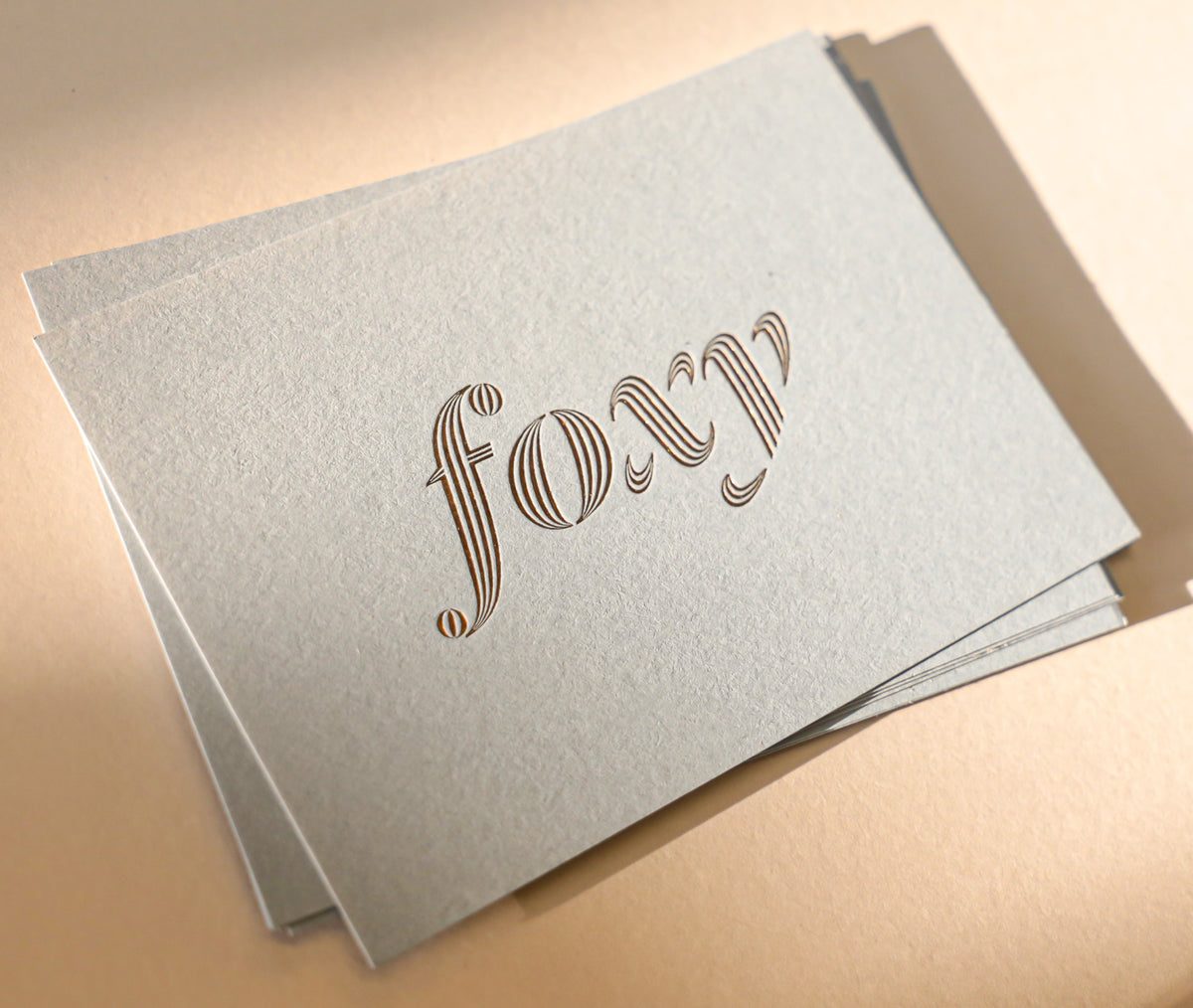 Stack of light gray greeting cards with 'foxy' text on a beige background