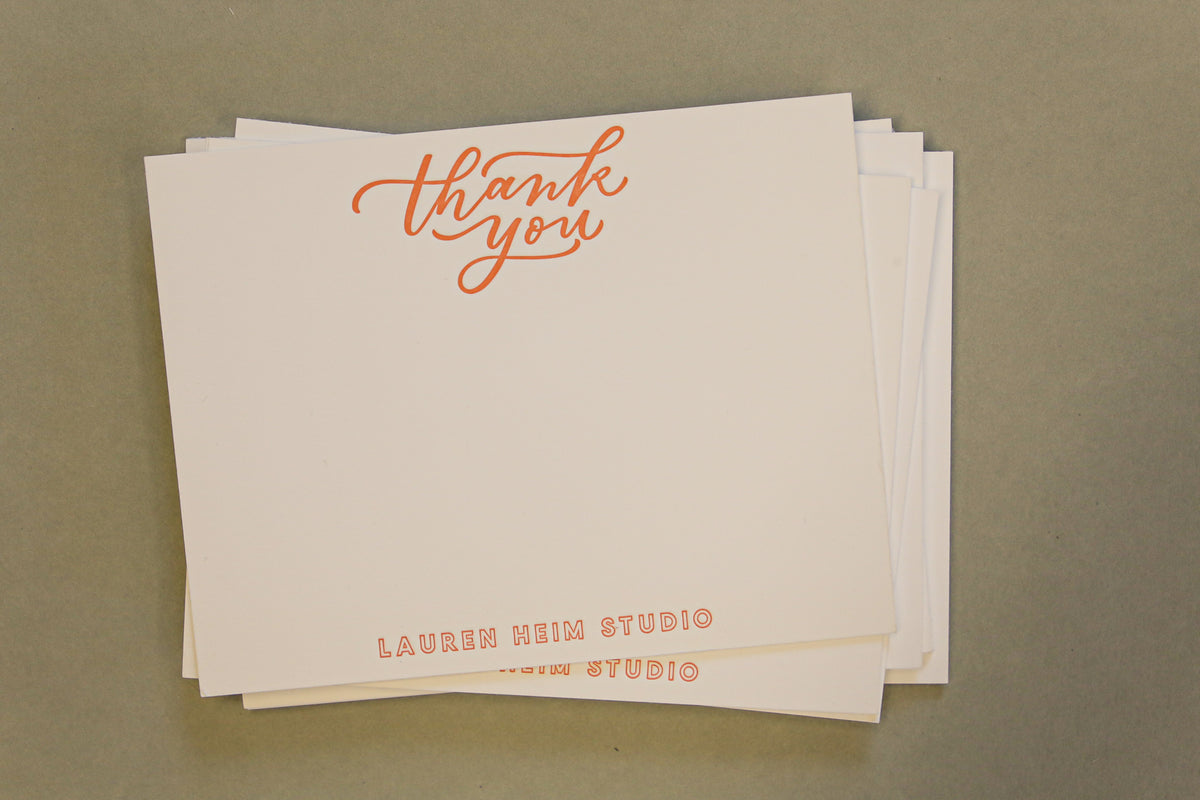 Stack of white cards with 'thank you' in orange text on a beige background