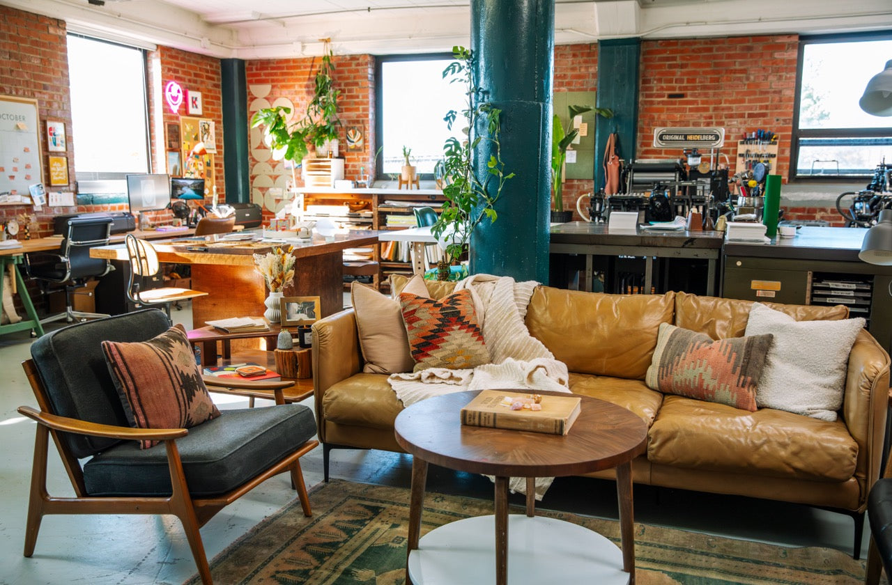 Modern office space/letterpress shop with a brown leather sofa, wooden chairs, and decorative elements.
photo by Alyssa Broadus